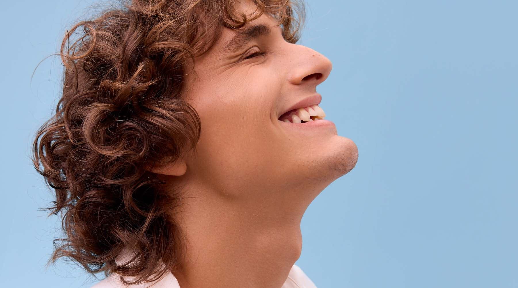 A person smiling with their eyes closed and their head tilted towards the sky, against a blue background.