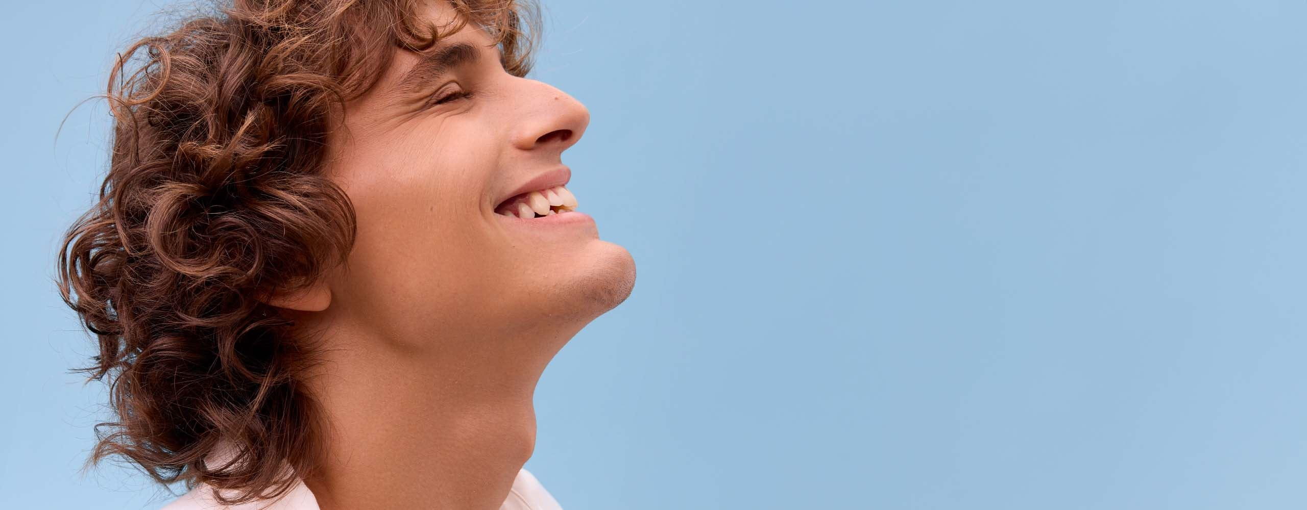 A person smiling with their eyes closed and their head tilted towards the sky, against a blue background.