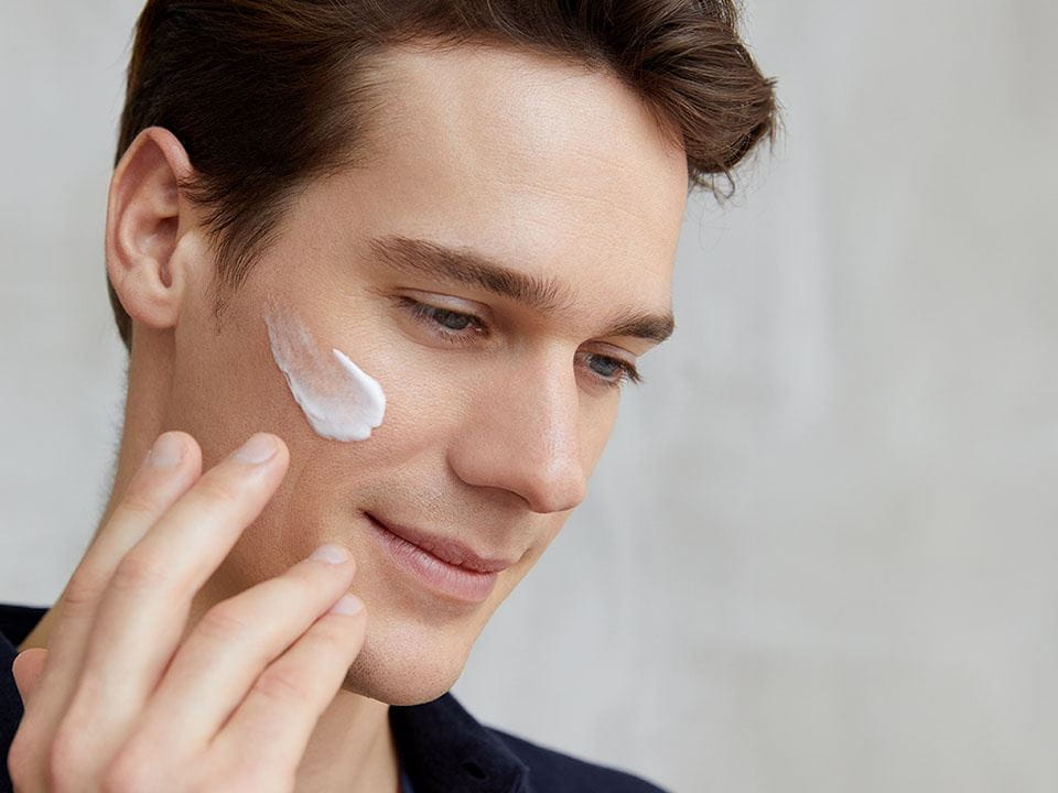 A man looking down with a swatch of moisturizer on his cheek