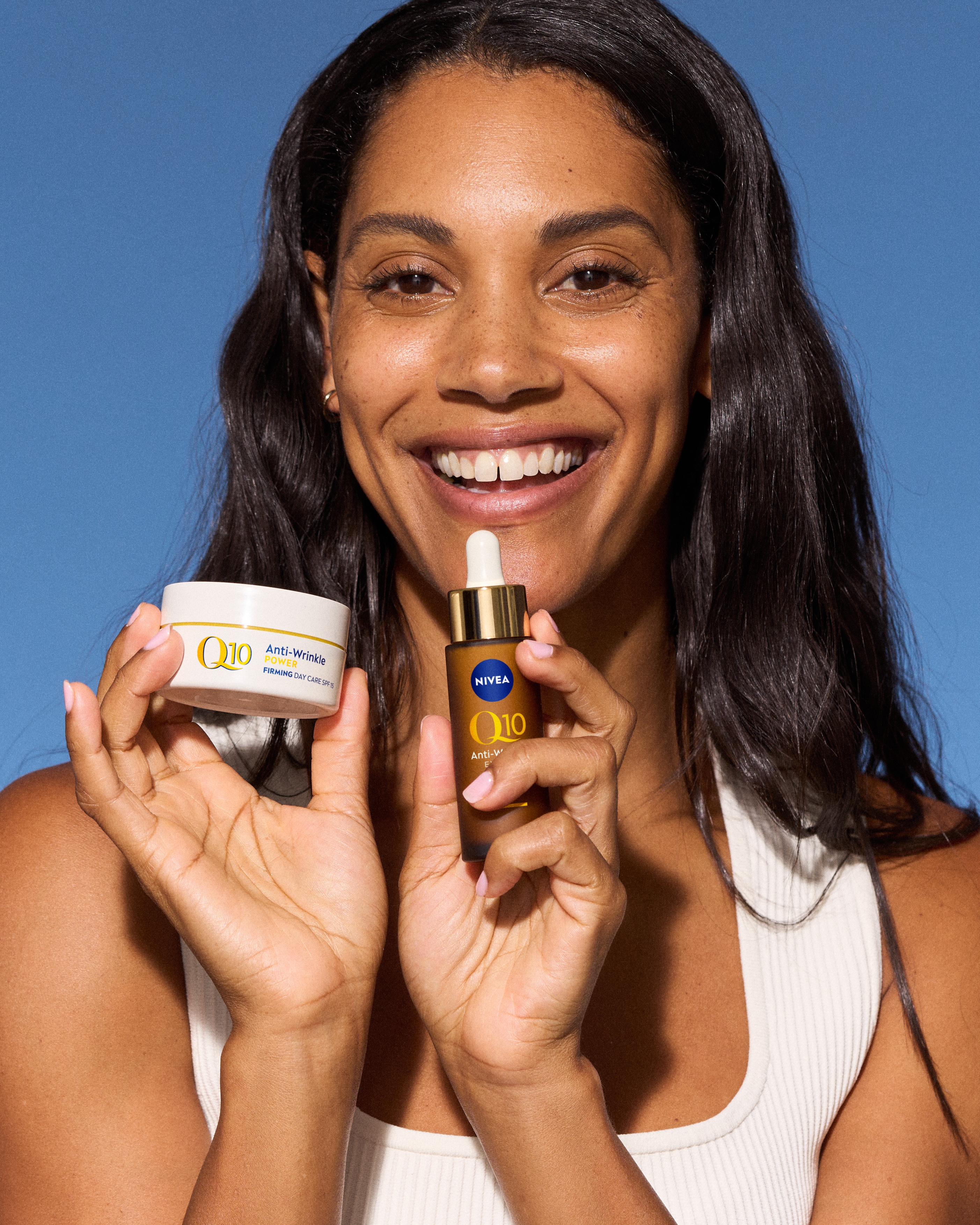 Person framför blå bakgrund, ler och håller upp NIVEA q10 dakräm och serum