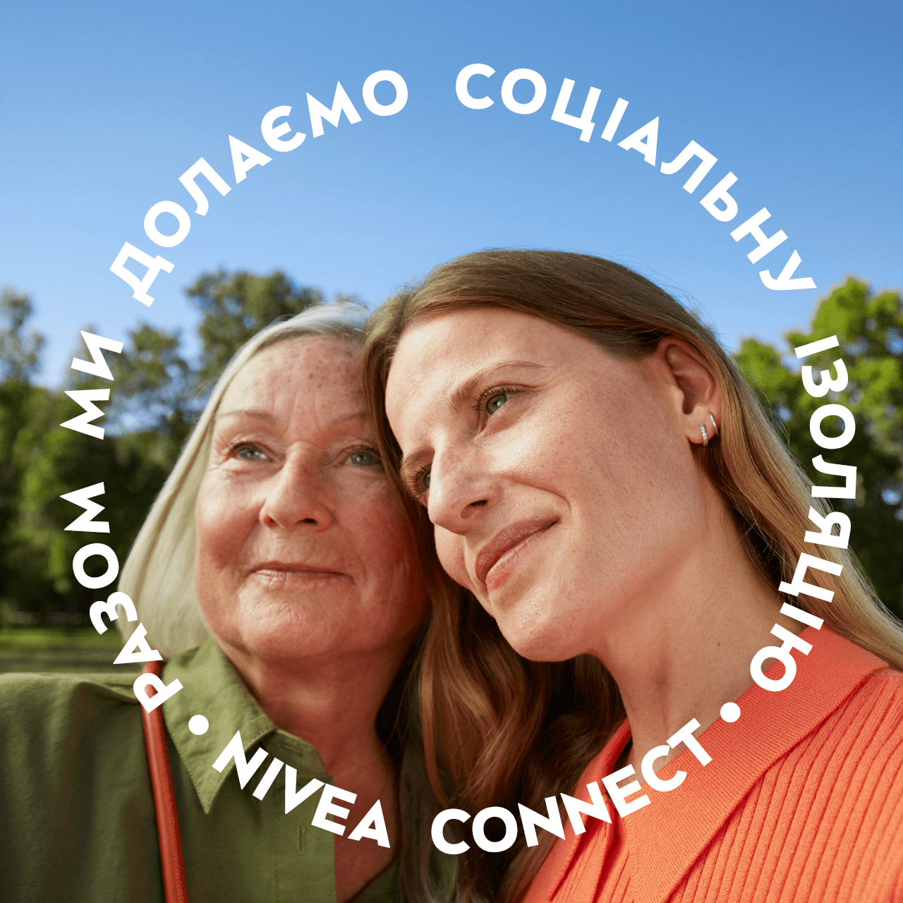Two women looking off-camera with a blue sky and trees in the background.