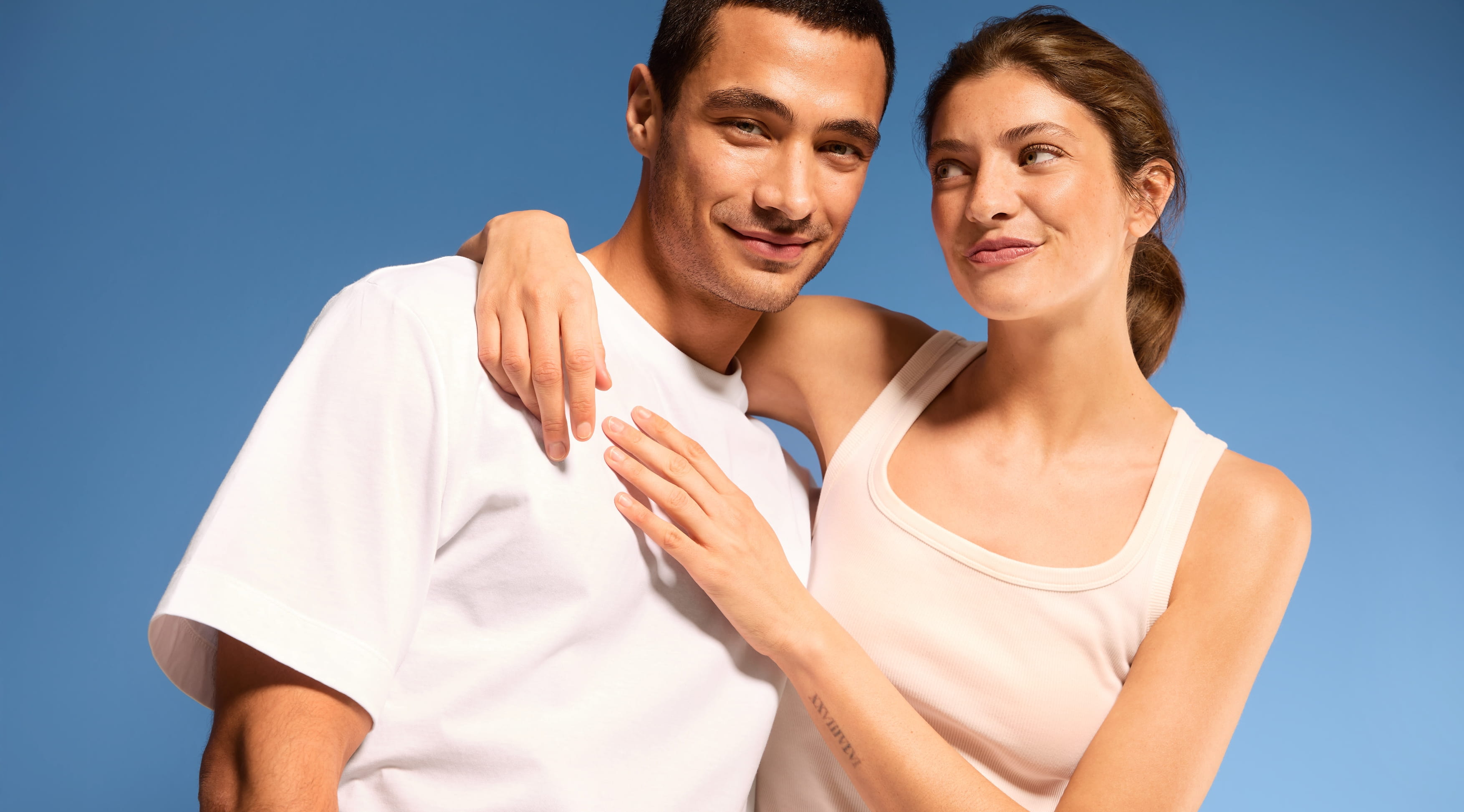 Man i vit t-shirt och kvinna i vitt linne, framför blå bakgrund