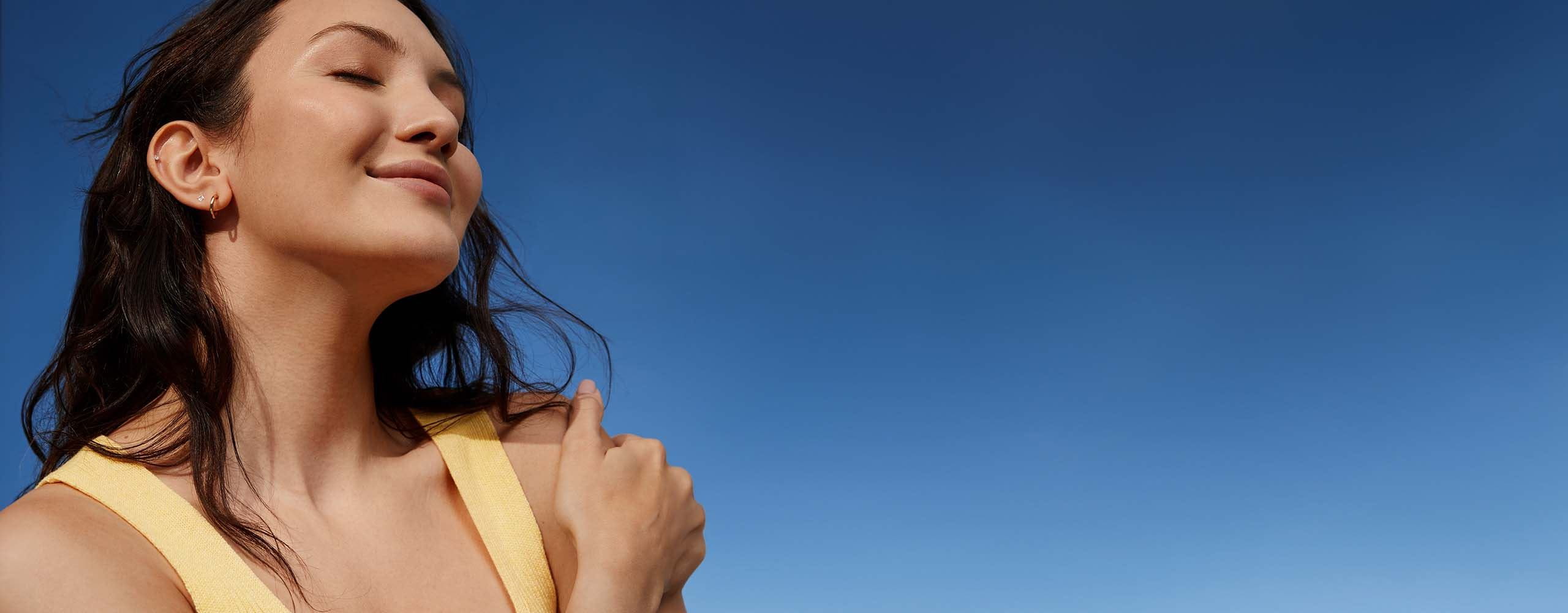 A person wearing a yellow coloured tank top is seen embracing themselves while smiling.