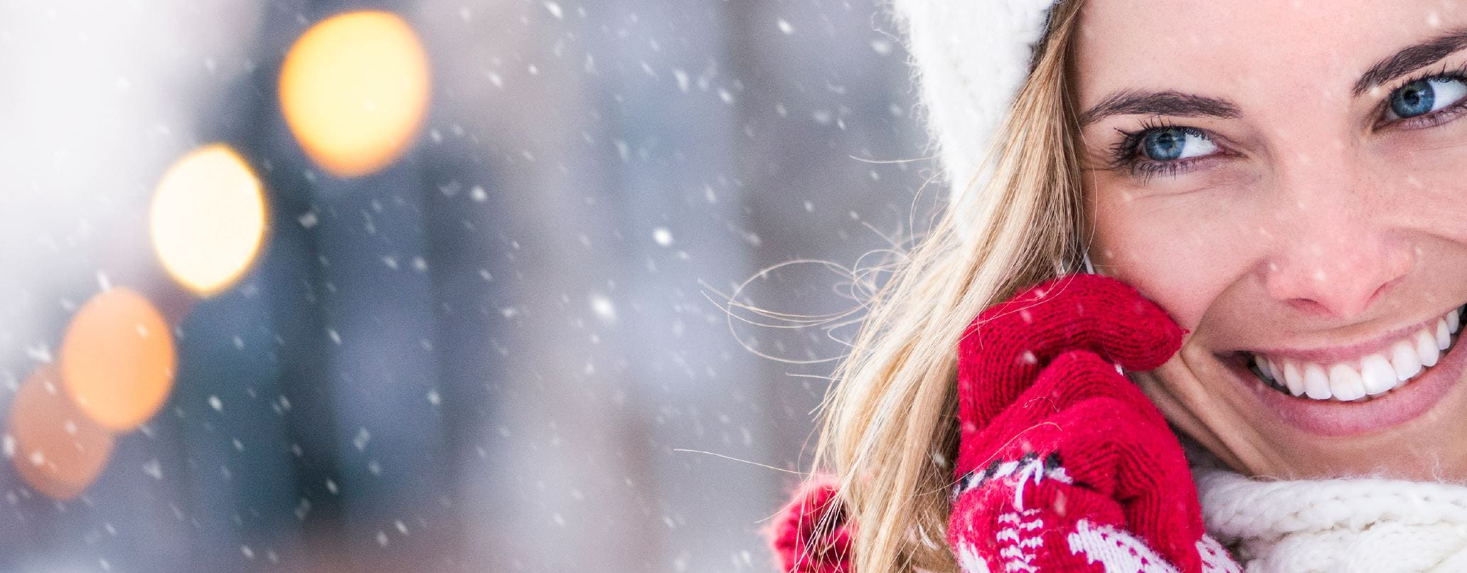 Image of a female model with blonde hair and blue eyes wearing red winter gloves with snow flurries shown behind and white font text inside a blue text box.