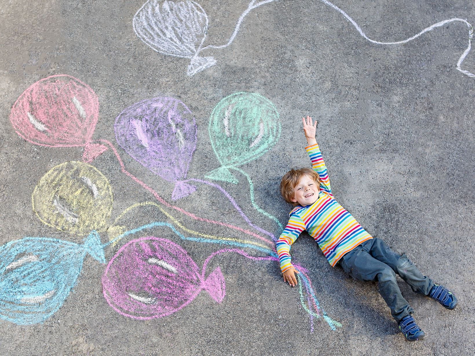 boy-having-fun-with-balloons-drawing-with-chalk-on-pavement