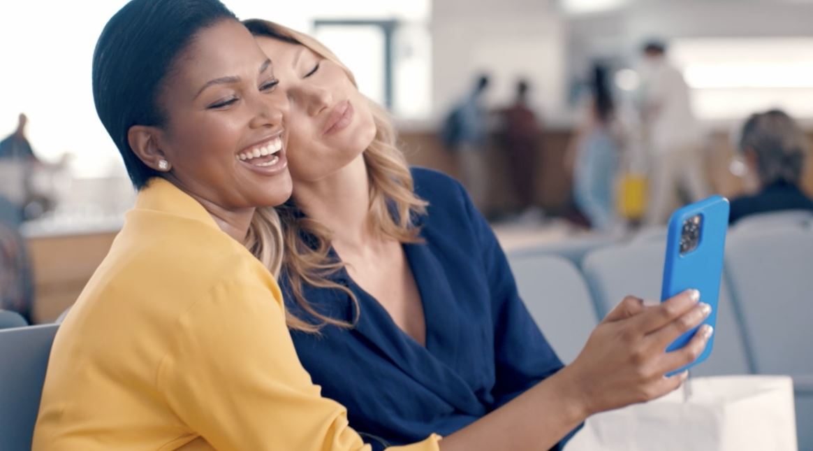 View of two female models smiling while holding a cell phone.