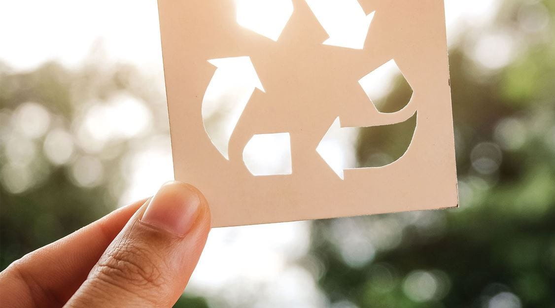 Ruka drži znak za recikliranje na svijetloj pozadini.