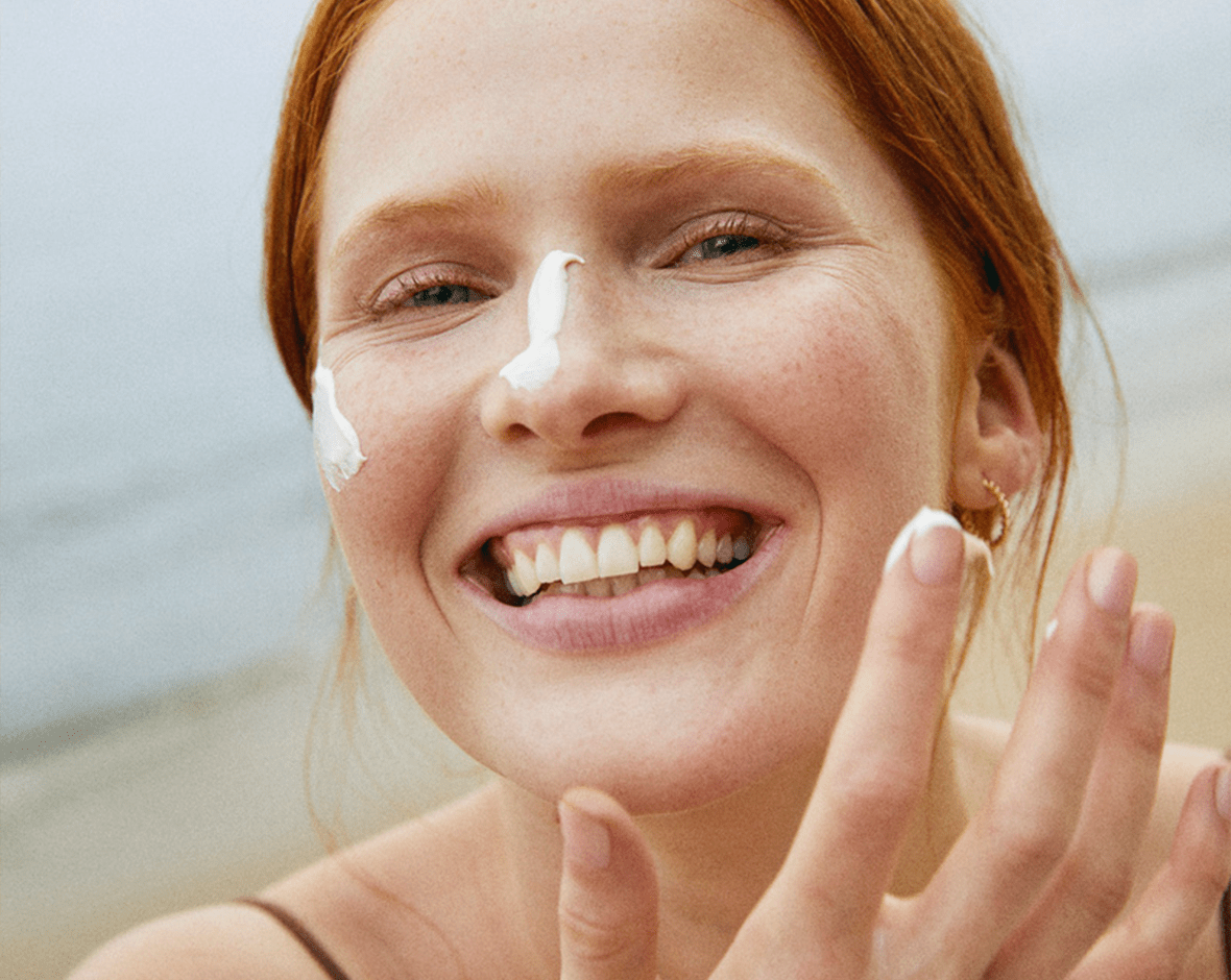 Persona sonriendo y colocándose crema en la cara