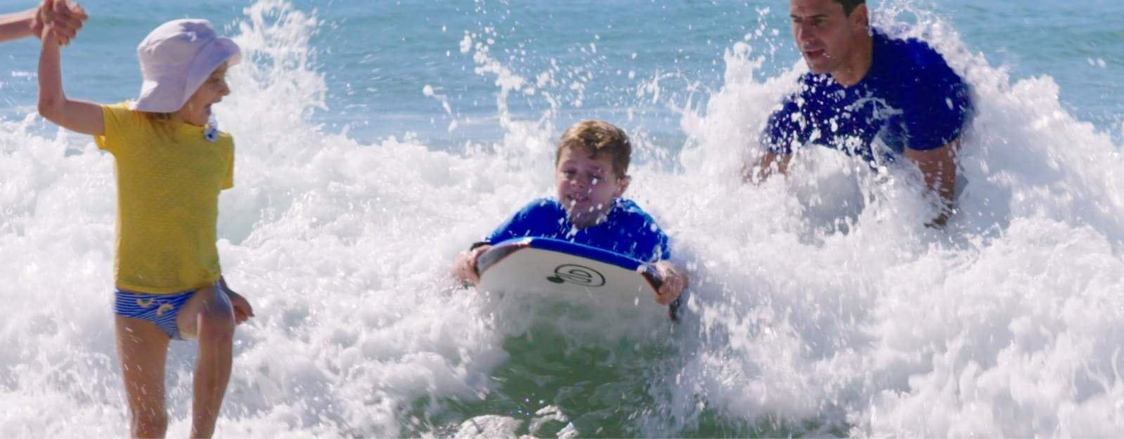 Parents with baby and child playing on beach with NIVEA Sunscreen
