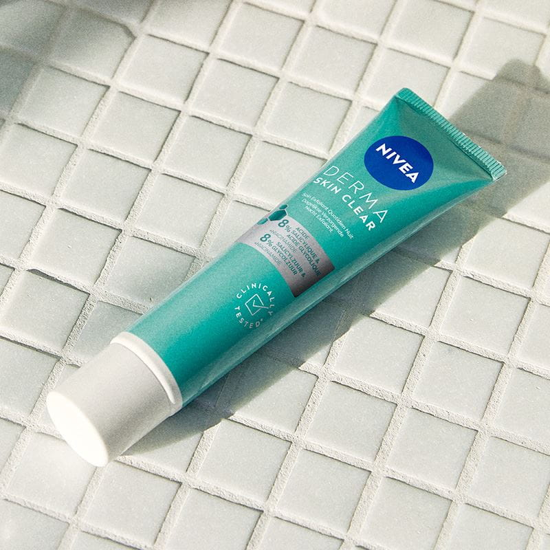 Nivea Derma Skin Clear Dagelijkse Verzorgende Nacht Exfoliant op een badkamermeubel naast een wasbak.