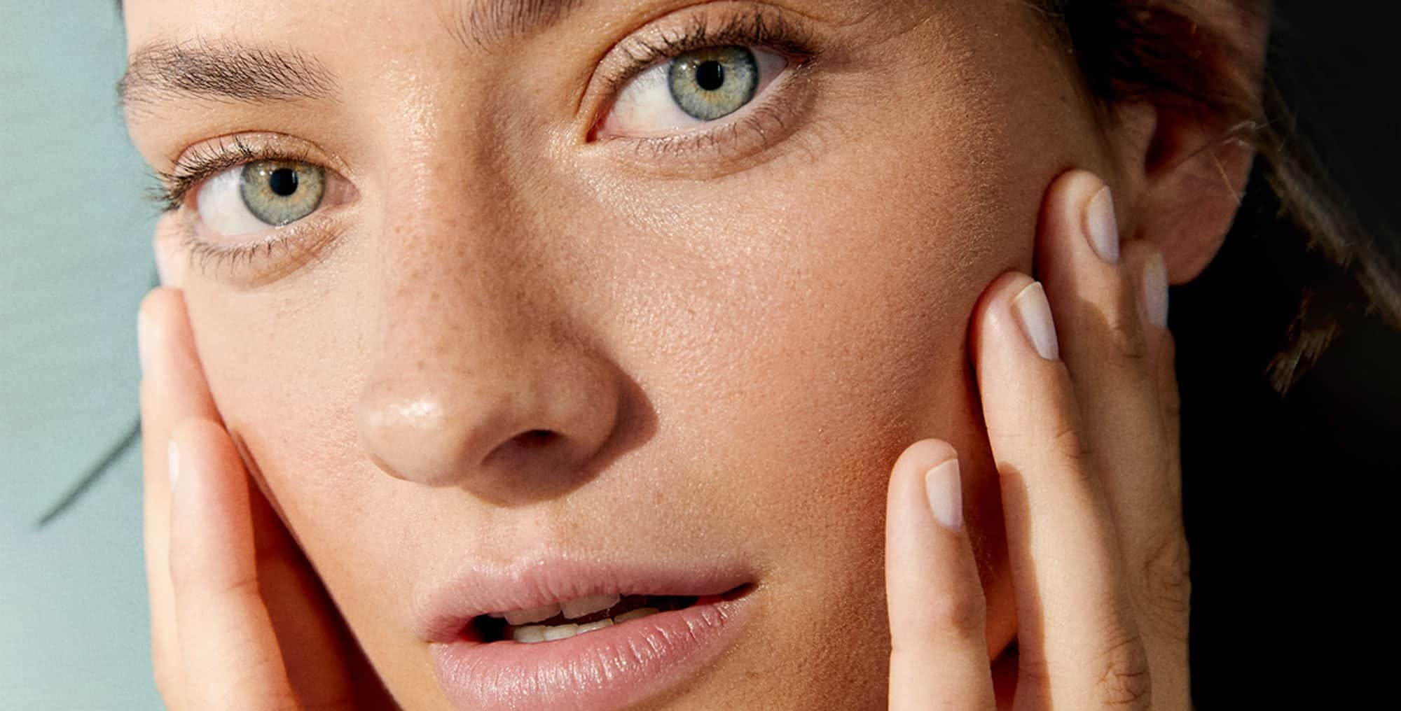 View of a female model with green eyes touching her face against a green background.