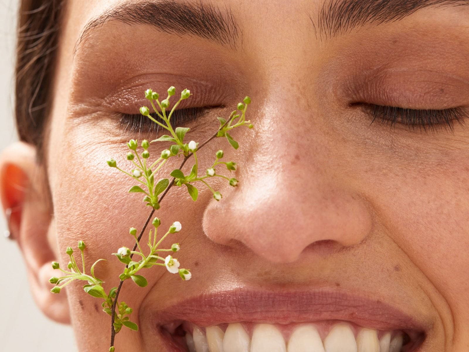 Close up view of a female model with her eyes closed and smiling with white flowers touching her face.