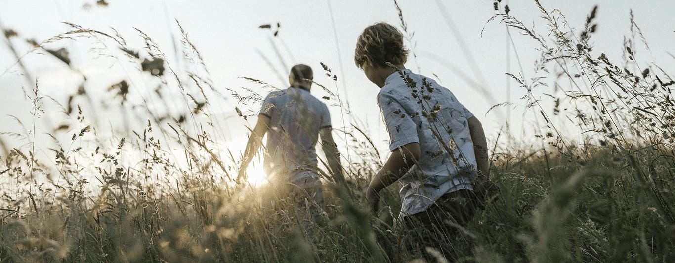 View of a man and a child walking through a field with greenery and plants surrounding them with the text Our Vision Climate Neutralized placed over top the image.