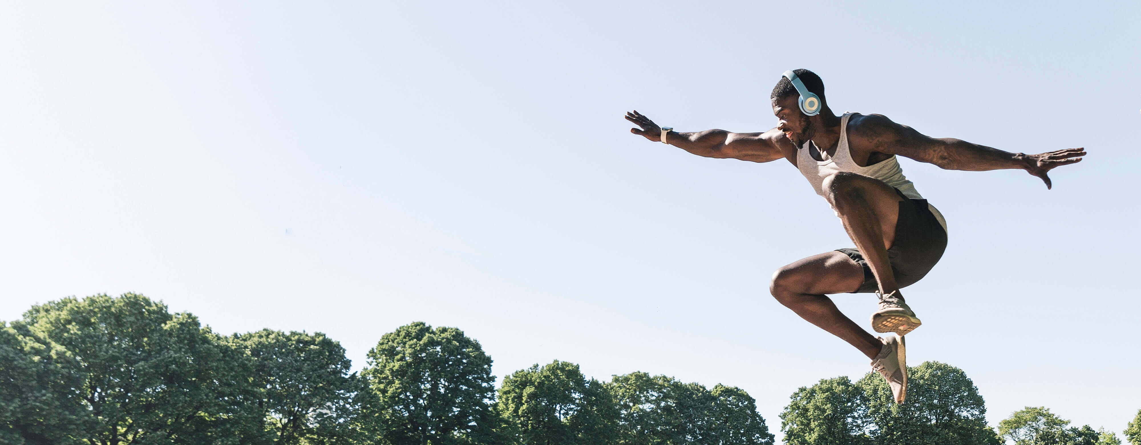 Mannequin masculin sautant dans les airs, bras déployés, écouteurs à la tête avec arbres en arrière-plan.