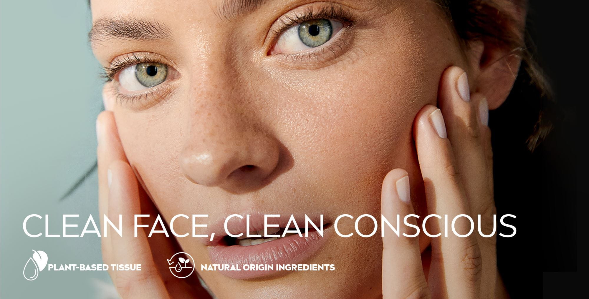 Close up view of a female model with green eyes touching her face against a green background.