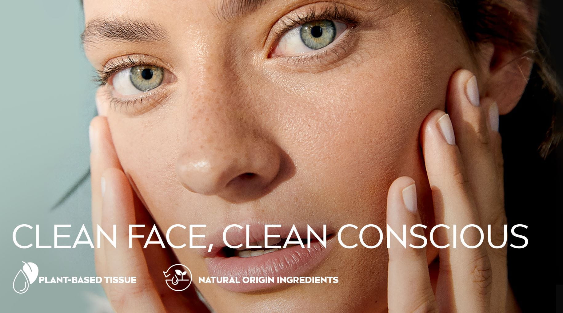 Close up view of a female model with green eyes touching her face against a green background.