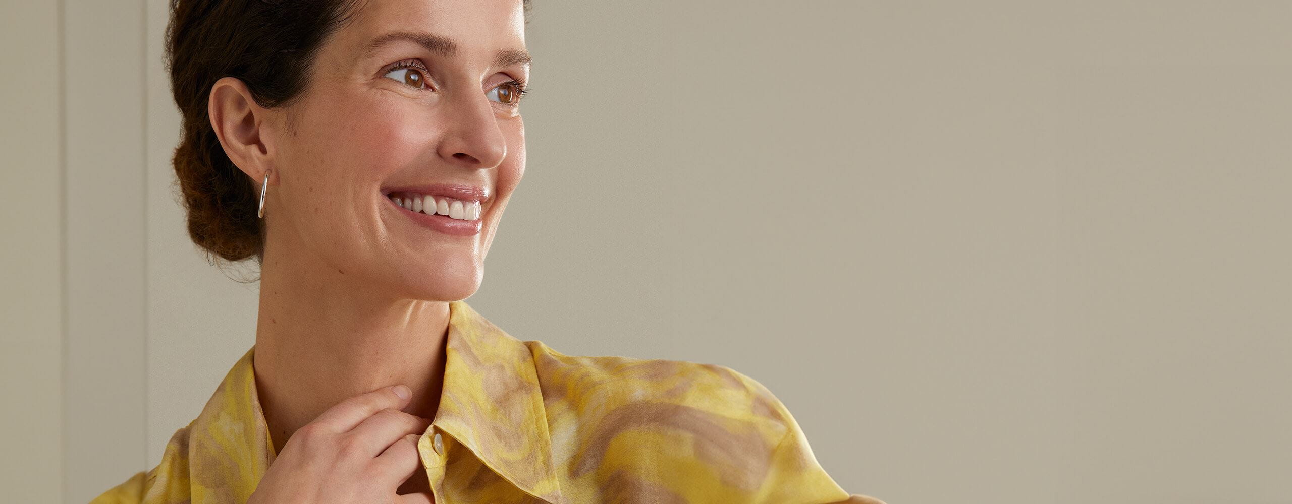 View of a person wearing a yellow coloured blouse, smiling while looking out into the distance.