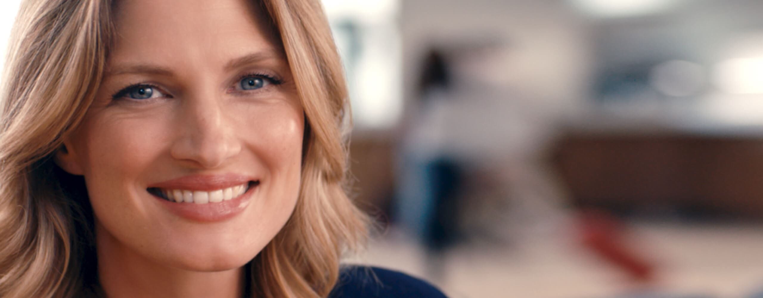 Une femme aux cheveux blonds et aux yeux bleus souriant avec un texte bleu apparaissant à droite à l
