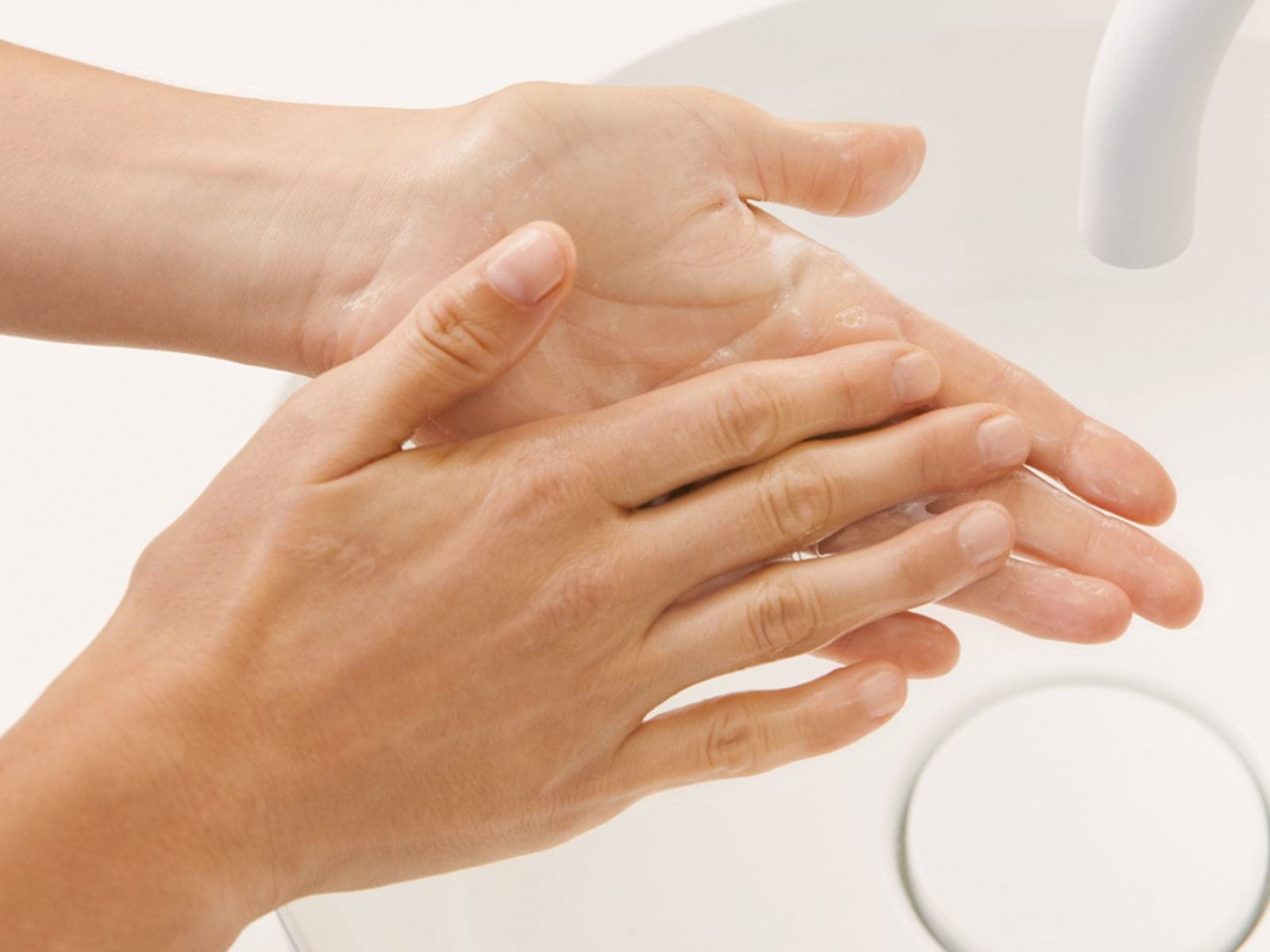 A closeup view of a person washing their hands in a white sink.