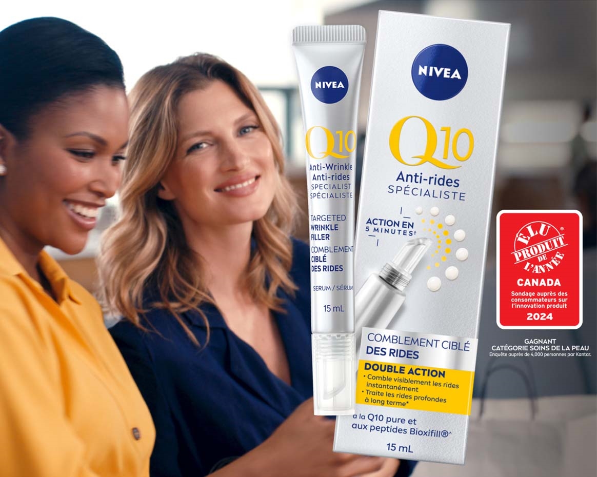 Vue de deux modèles féminins souriant tout en tenant un téléphone portable avec le produit NIVEA Q10 Anti-rides Spécialiste Comblement ciblé des rides placé au-dessus d’un fond bleu.