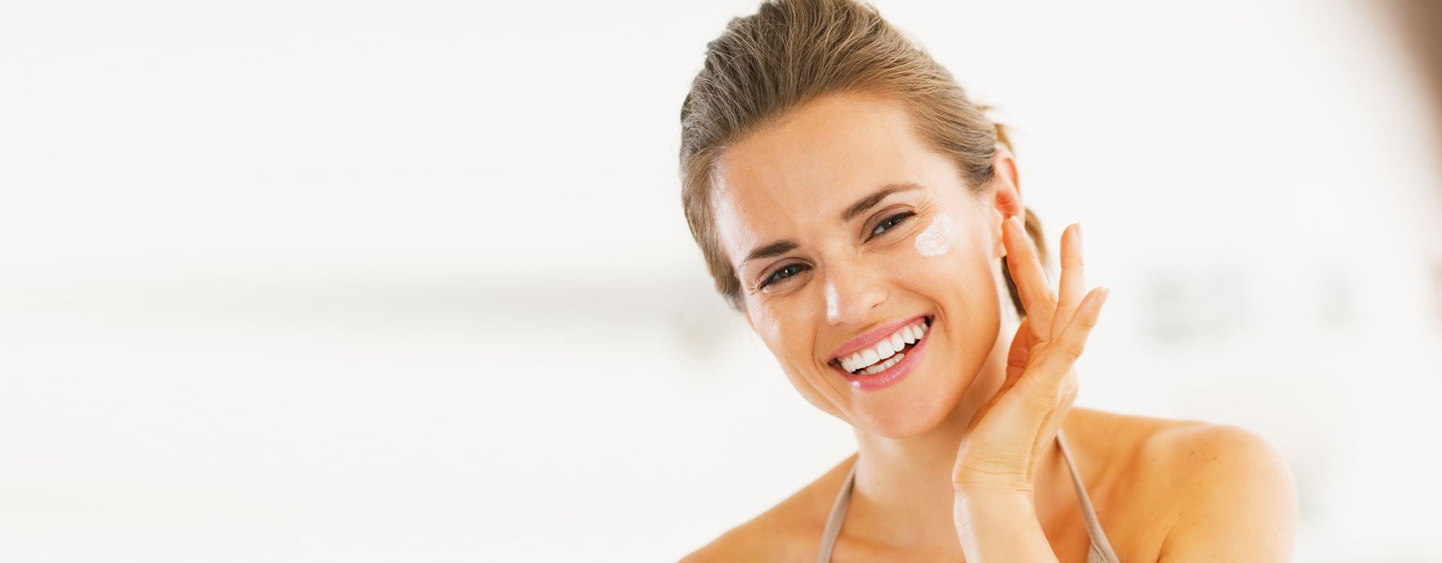 Frau cremt ihr Gesicht mit Sonnencreme ein