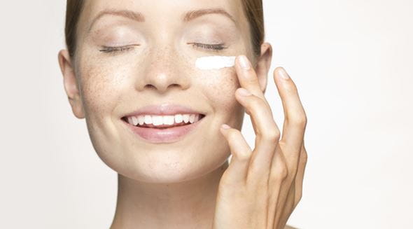 Femme rouse se mets de la crème sur la joue