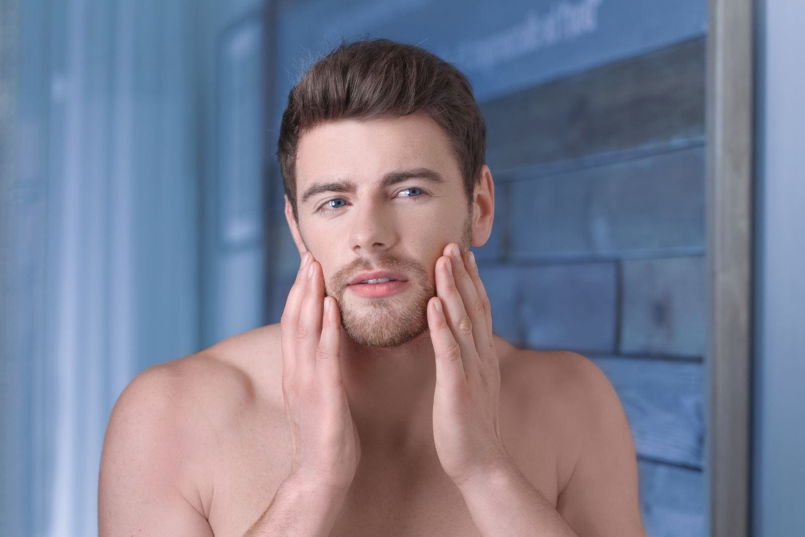 man looking himself in the mirror and touching his beard