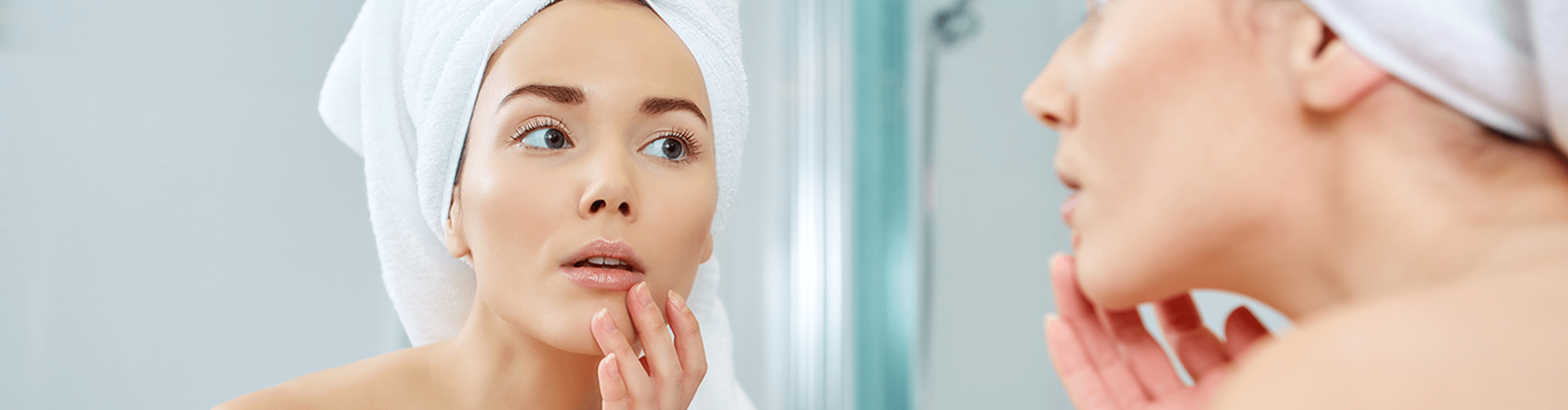 woman touching her face while looking herself in the mirror