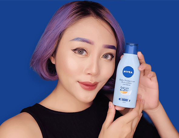 woman with purple hair holding NIVEA SUN body lotion