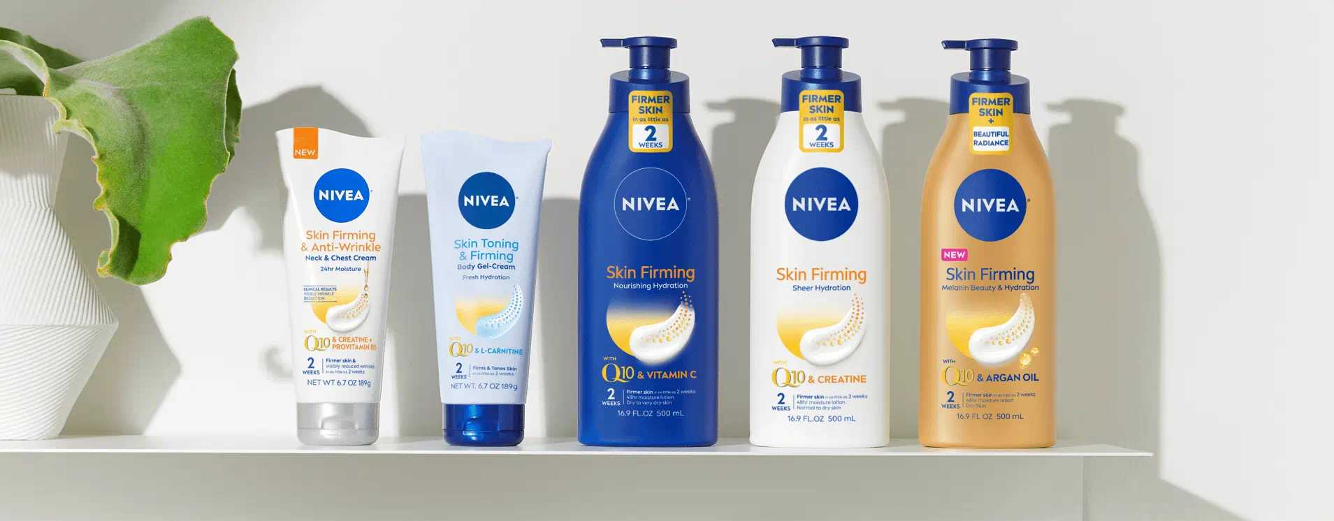 5 Nivea products are lined up on a shelf. There is a plant in a white ceramic vase on the furthermost left side. Next to the plant are 5 Nivea products. In line-up order these products are: NEW NIVEA Skin Firming & Anti-Wrinkle Neck & Chest Cream with Q10, NIVEA Skin Toning & Firming Gel-Cream with Q10 & L-Carnitine, NIVEA Skin Firming Nourishing Hydration Body Lotion with Q10 & Vitamin C, NIVEA Skin Firming Sheer Hydration Body Lotion with Q10 & Creatine and NEW NIVEA Skin Firming Melanin Beauty & Hydration Body Lotion with Q10